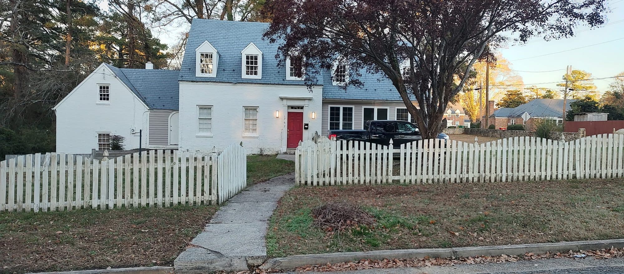 White brick Cape Cod house with dormers, a red front door and a picket fence